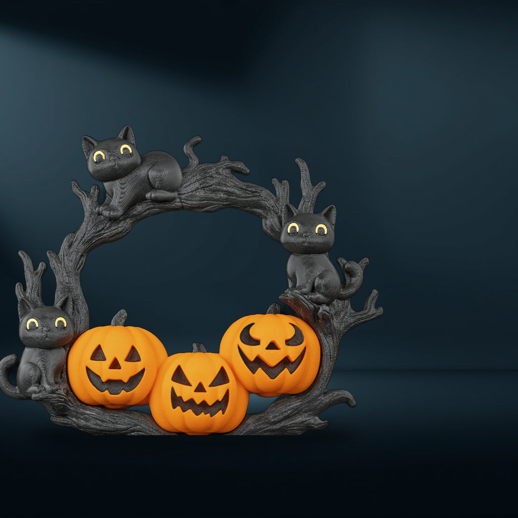 Halloween-Türkranz mit drei schwarzen Katzenfiguren und drei Gruselkürbissen auf Astwerk, Frontalansicht vor dunklem Studiohintergrund mit sanftem Spotlight