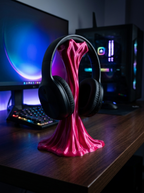 Pinker Sticky-Splash Headset-Ständer mit aufgesetztem Over-Ear-Kopfhörer, Frontalansicht auf dunklem Schreibtisch mit Monitor im Hintergrund