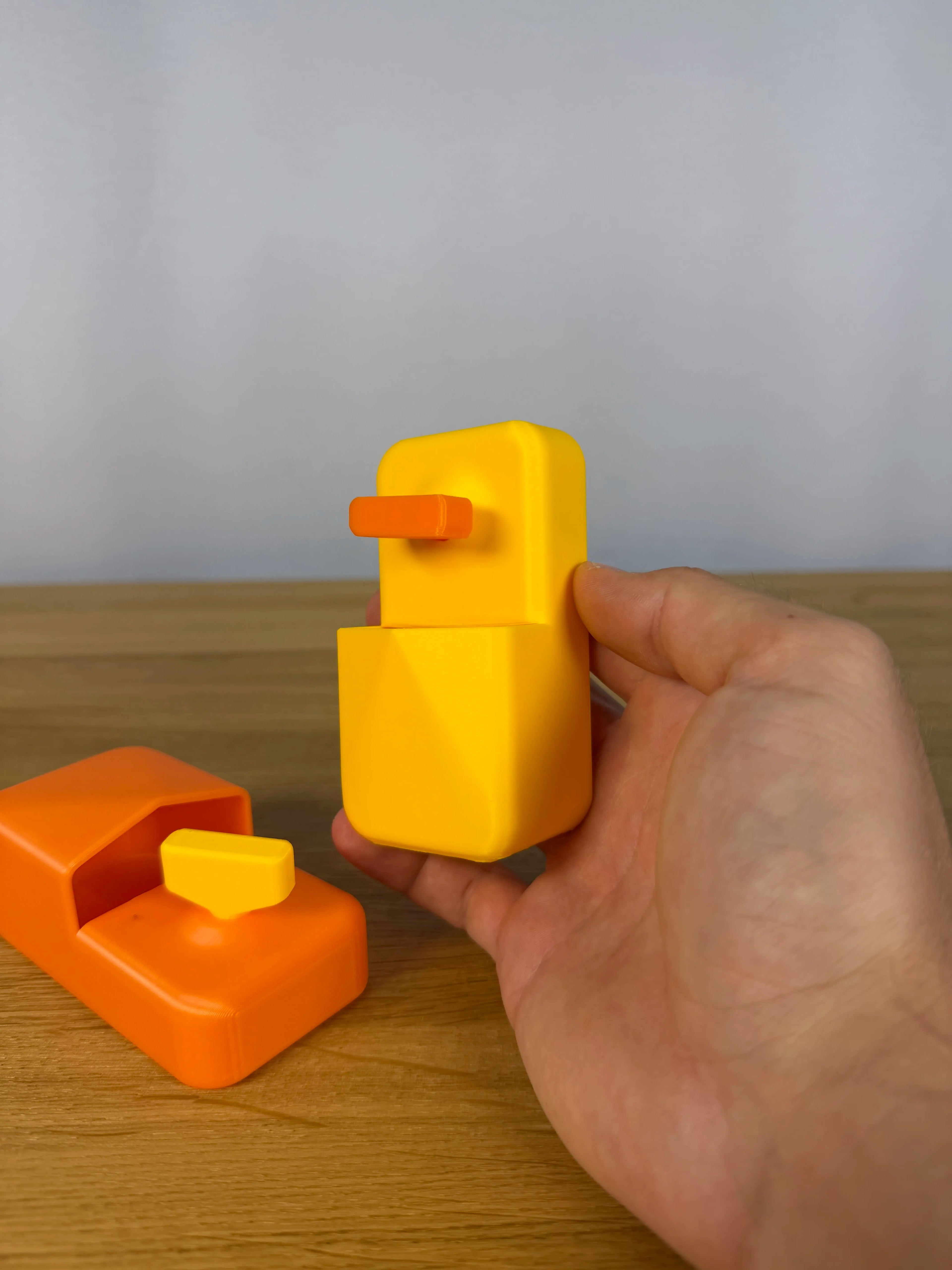 Hand hält gelbe Halterung mit orangem Entlüftungsschlüssel, im Hintergrund die zweite Farbkombination in Orange mit gelbem Schlüssel auf Holztisch