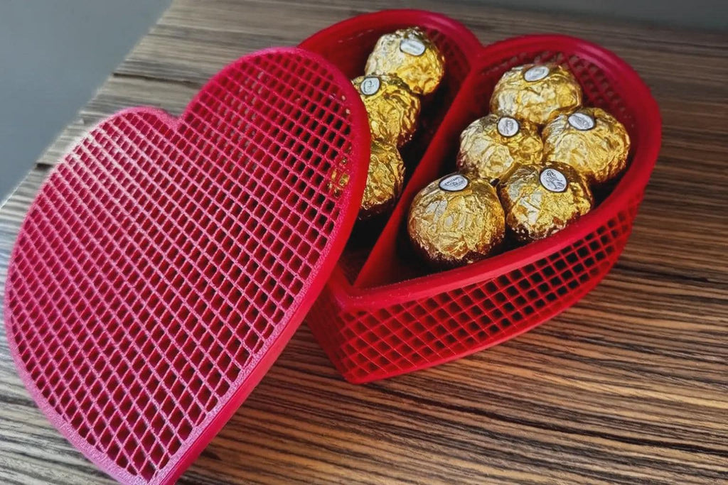 Rote Gitter-Herzbox geöffnet mit goldfolierten Pralinen befüllt, nur eine Farbvariante gezeigt, auf Holztisch