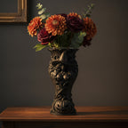 Schwarze Hexen-Kürbis-Vase gefüllt mit einem Strauß frischer orangefarbener Dahlien und dunkelroter Rosen in Wasser, vor dunklem Wandrahmen