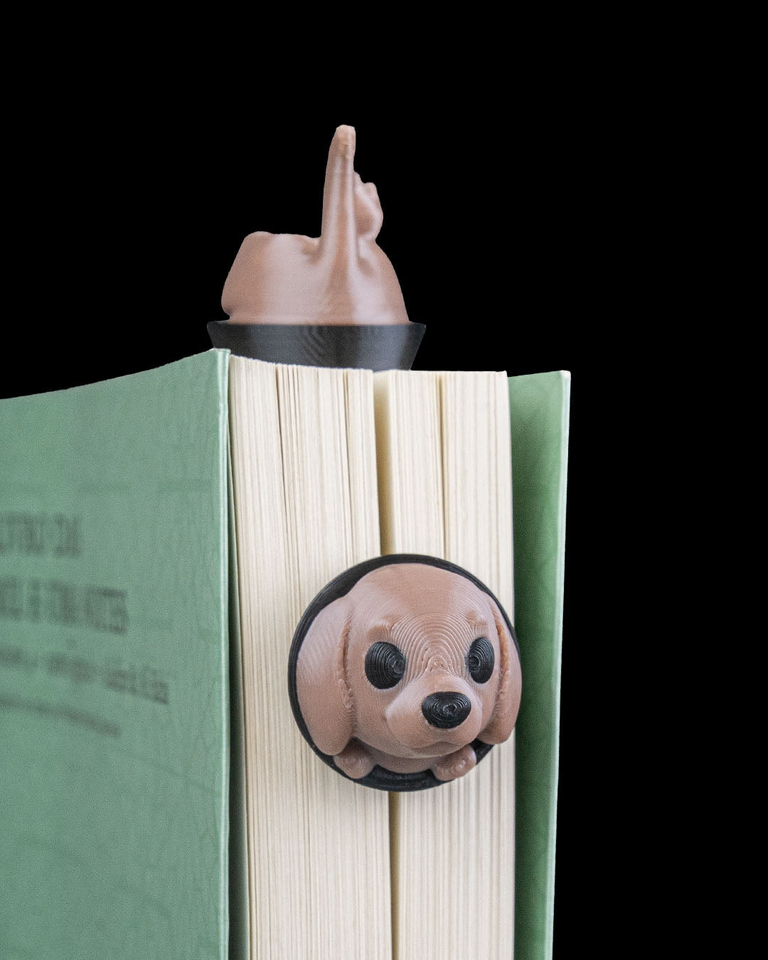 Braunes Hunde-Lesezeichen auf grünem Buch geklemmt, Hinterteil ragt oben aus den Buchseiten, runder Kopf mit Schlappöhren und Kulleraugen unten an der Buchkante