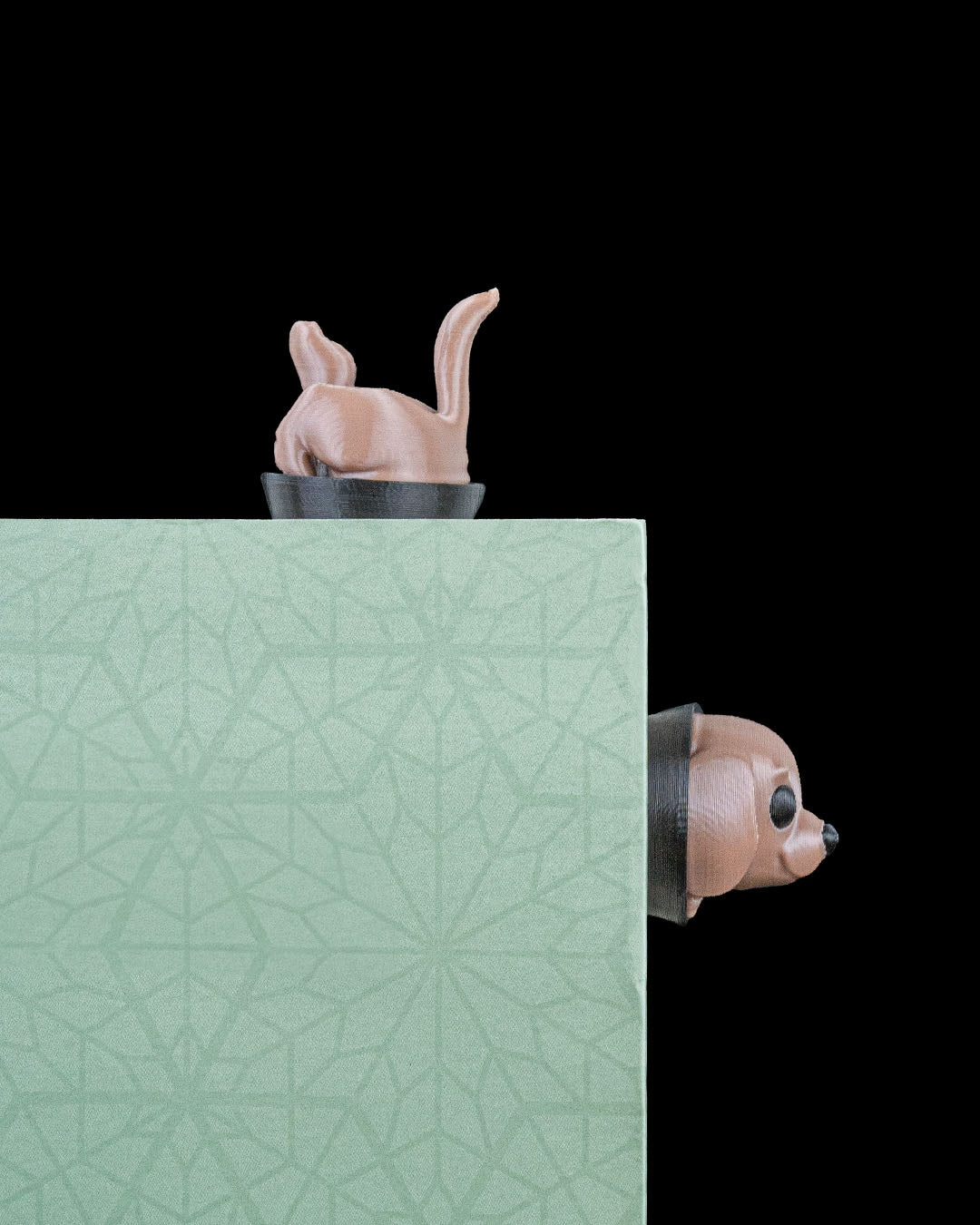 Braunes Hunde-Lesezeichen auf der Ecke eines grün gemusterten Buchdeckels geklemmt, Hinterteil oben und Kopf seitlich sichtbar, schwarzer Hintergrund