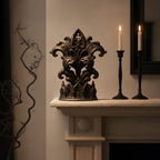 Gothic-Kathedralen-Skulptur mit Fleur-de-Lis-Blattranken in Mattschwarz auf einem hellen Kaminsims, daneben zwei schwarze Kerzenständer mit brennenden Kerzen