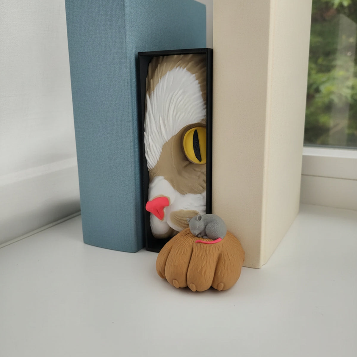 Katzen-Buchstütze mit Maus Book Nook auf weißem Fensterbrett zwischen zwei schlichten Büchern, Tageslicht und Blick ins Grüne im Hintergrund