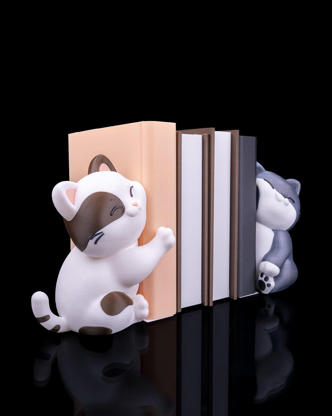 Katzen-Buchstützen-Paar mit Büchern dazwischen aus leicht gedrehtem Blickwinkel, freigestellt vor schwarzem Hintergrund