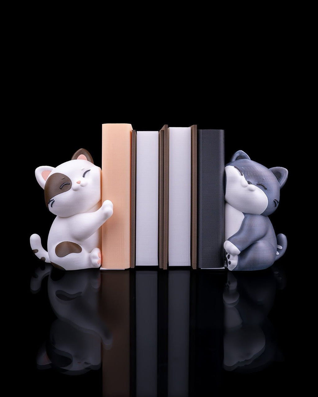 Katzen-Buchstützen-Set: weiß-braune und graue Katzenfigur halten fünf Bücher (pfirsich, weiß, dunkelgrau) zwischen sich, Frontalansicht vor schwarzem Hintergrund