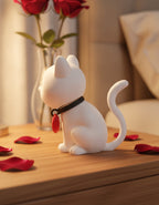 Weiße Katze der Katzen-mit-Herz-Figur auf Nachttisch mit Rosenvase im Hintergrund, Seitenansicht mit rotem Herz-Anhänger am Halsband – Münch3D 3D-Druck