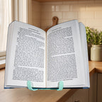 Buchständer mit aufgeschlagenem Buch (Huckleberry Finn) von vorne, Textseiten symmetrisch und gut lesbar. Im Hintergrund Kochbücher und Vorratsdosen auf der Küchenarbeitsplatte.
