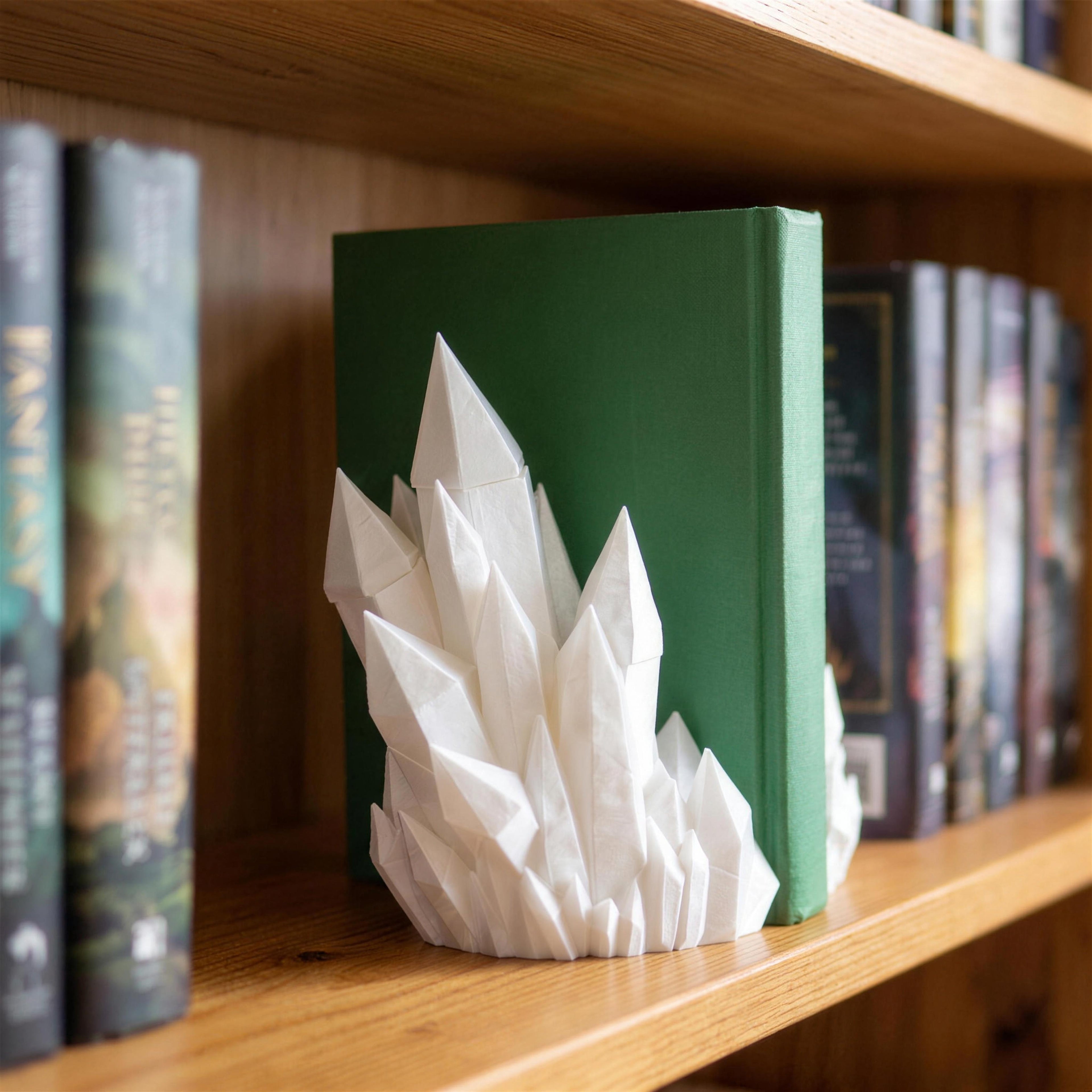 Weiße Kristall-Buchstütze mit spitzen, facettierten Kristallzacken steht auf einem Holzregal vor einem aufrecht stehenden grünen Buch, links und rechts weitere Bücher mit bunten Buchrücken.
