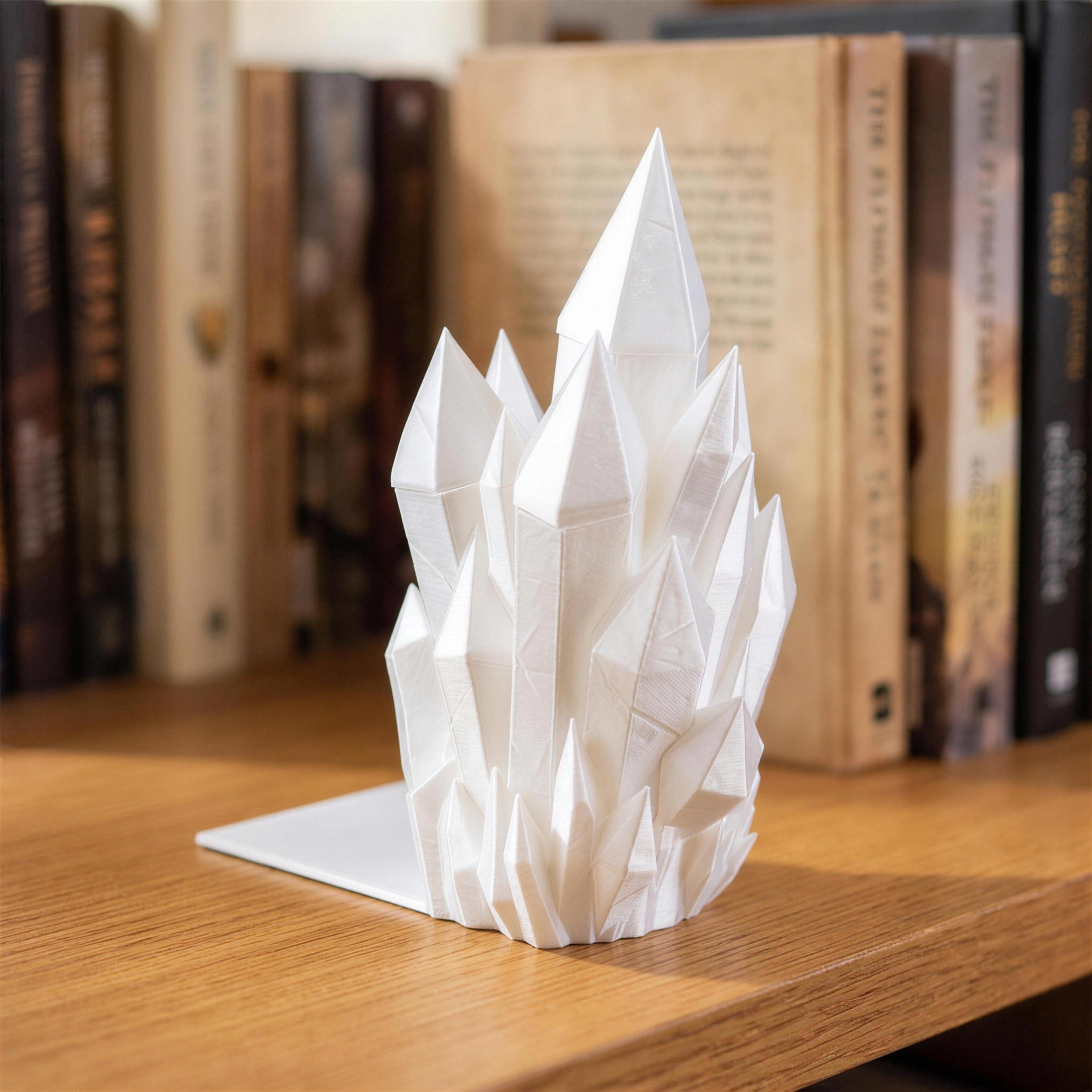 Weiße Kristall-Buchstütze mit mehreren spitzen Kristallzacken in Nahaufnahme, steht auf einer Holzablage vor einem aufrecht stehenden Buch mit cremefarbenem Seitenschnitt, im Hintergrund weitere Bücher.