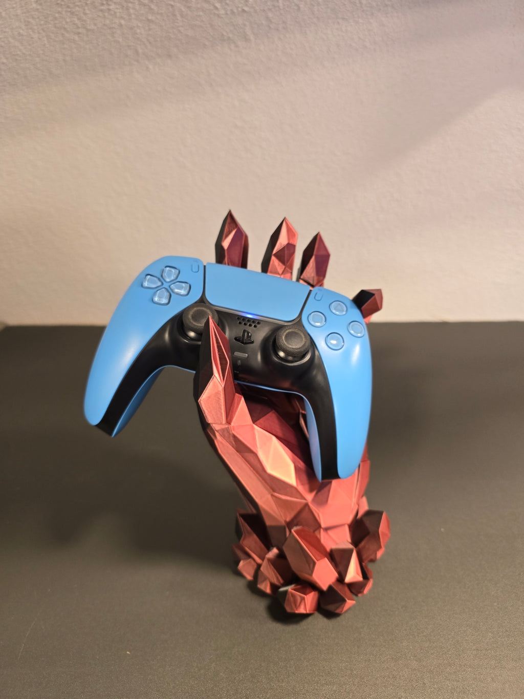 Kristallhand-Controllerhalter in Kupfer-Rot mit eingesetztem blauem Gaming-Controller, Frontalansicht vor Wohnzimmerwand