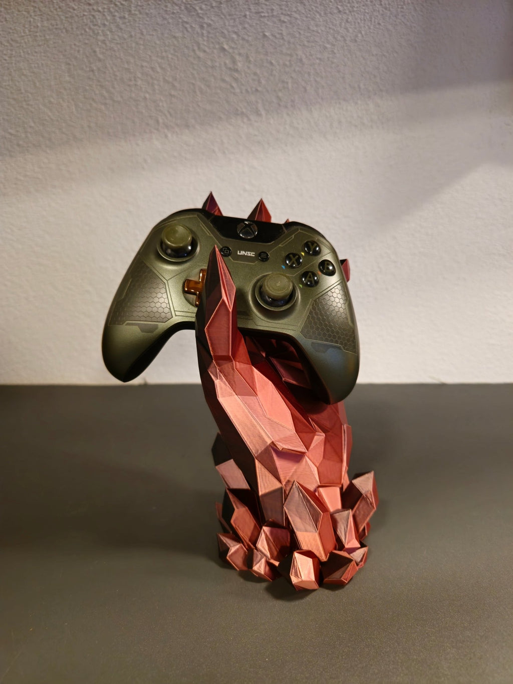 Kristallhand-Controllerhalter in Kupfer-Rot mit eingesetztem olivgrünem Gaming-Controller, Nahaufnahme mit sichtbaren Steuerkreuz-Details