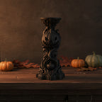 Schwarzer Kürbis-Kerzenhalter mit grinsendem Kürbisgesicht auf gotischer Flammensäule, Frontalansicht mit Herbstdeko im Hintergrund
