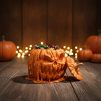 Geöffnete schmelzende Kürbis-Box mit Süßigkeiten gefüllt, Deckel lehnt seitlich an der Box, auf herbstlich dekoriertem Holztisch mit Lichterkette im Hintergrund
