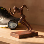 Läufer-Statue in Kupfer-Bronze-Optik auf Holzregal, Seitenansicht der Sprint-Pose, unscharfer Hintergrund mit Laufschuh und Stoppuhr – Münch3D