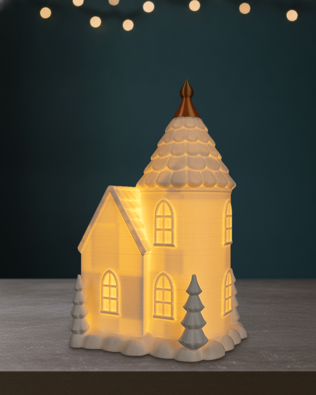 Leuchtendes Turmhaus von der Rückseite mit Rundturm und warm erleuchteten Fenstern, auf einem dunklen Steintisch vor einer petrolfarbenen Wand mit Lichtpunkten