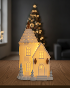 Leuchtendes Turmhaus in Weiß und Gold auf einem Eichentisch, im Hintergrund ein unscharf beleuchteter Weihnachtsbaum