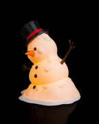 LED-Tischlampe Schneemann mit Zylinderhut und Kohle-Knöpfen, Frontalansicht aus leicht anderem Blickwinkel mit warmem LED-Licht, vor schwarzem Hintergrund