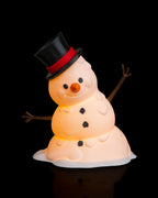 LED-Tischlampe Schneemann mit Zylinderhut, Kohle-Knöpfen und Astarmen, Frontalansicht mit warmem LED-Licht, vor schwarzem Hintergrund