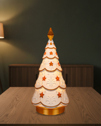 Leuchtender Weihnachtsbaum im Ornament-Design in der Seitenansicht, warm von innen beleuchtet, auf einem Holztisch vor einer grünen Wand mit Sideboard und Lampenlicht