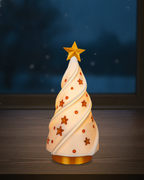 Leuchtender Weihnachtsbaum im Spiral-Design mit goldenem Stern auf goldenem Sockel, warm von innen beleuchtet, auf einer dunklen Fensterbank vor einem Fenster am Abend mit Schneeflocken