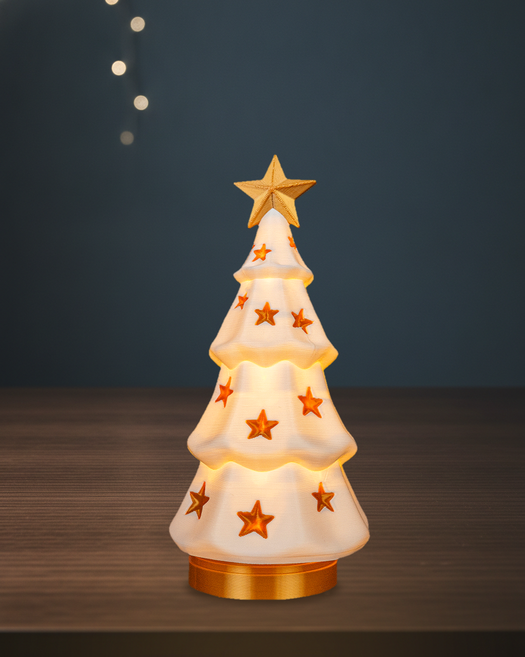 Leuchtender Weihnachtsbaum im Stufen-Design mit goldenen Sternen, goldenem Stern als Spitze und goldenem Sockel, warmes LED-Licht scheint durch den weißen Baum, auf einem dunklen Holztisch vor blauer Wand mit Lichterketten-Bokeh