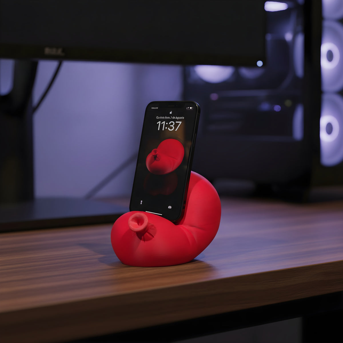 Roter Luftballon-Handyhalter mit eingestecktem Smartphone auf dunklem Walnuss-Gaming-Schreibtisch, PC-Tower mit blau-violettem RGB-Glanz im Hintergrund
