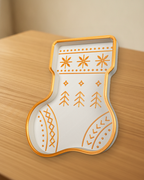 Weiß-goldene Nikolausstiefel-Schale in schräger Ansicht auf einem Holztisch mit goldenem Rand und Strickmuster, im Hintergrund weiches Fensterlicht
