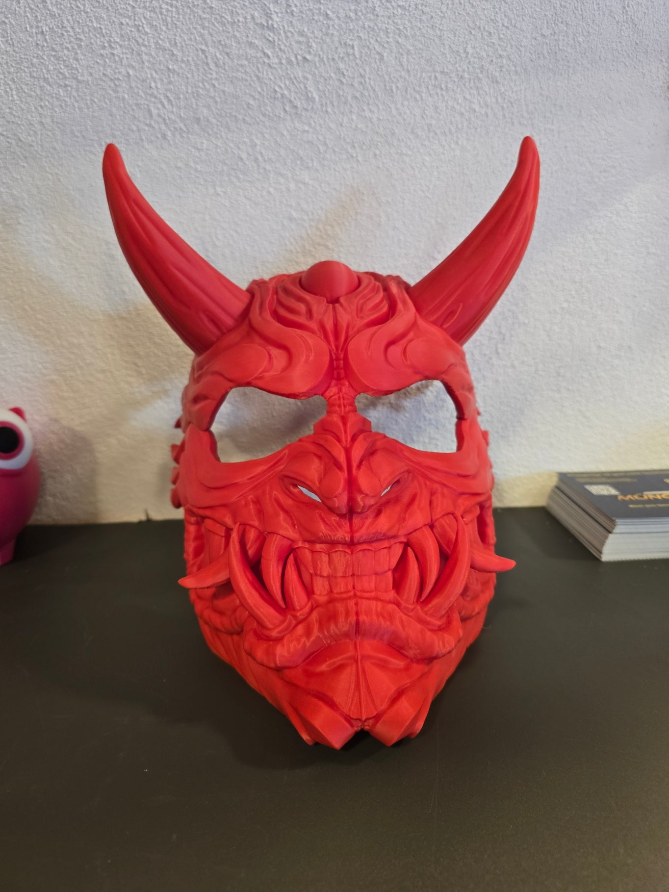 Oni-Maske Der Dämon in Rot, zentrale Frontalansicht mit aufragenden Hörnern vor weißer Wand – Münch3D
