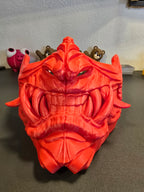 Oni-Maske Der Dämon in Rot, Ansicht von unten mit Fokus auf Maul und Reißzähnen, Deko-Figuren im Hintergrund – Münch3D