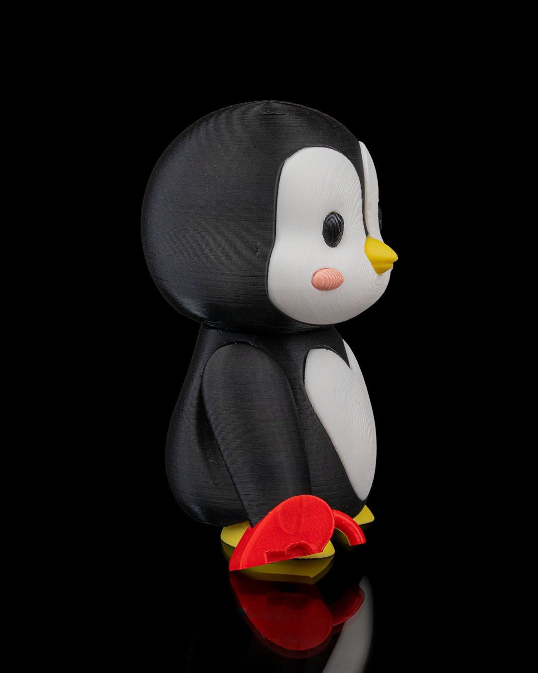 Einzelne Pinguin-Figur von hinten-seitlich fotografiert, rote Herzschloss-Hälfte liegt am Boden neben den gelben Füßen, schwarzer Hintergrund