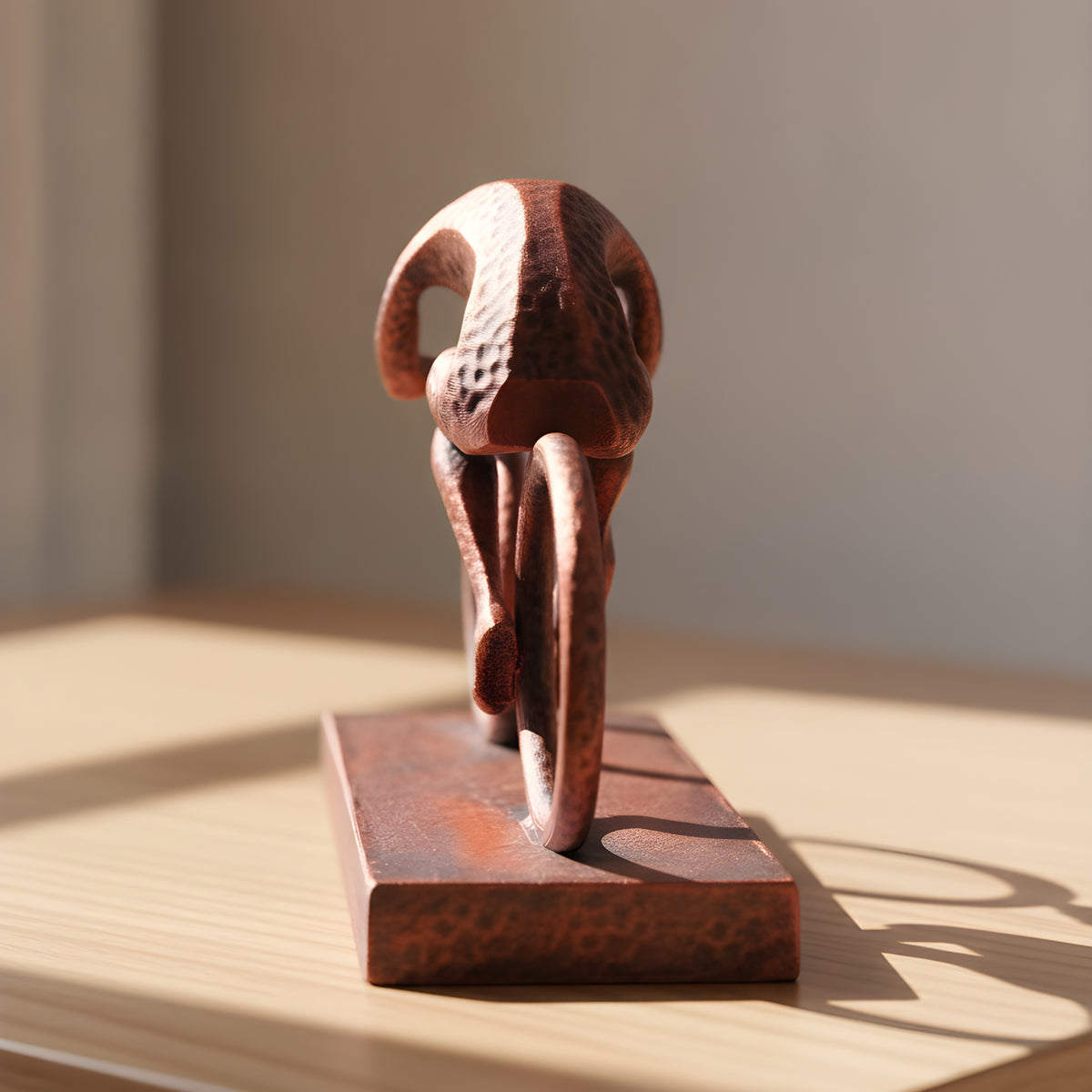 Radfahrer-Statue in Kupfer-Bronze-Optik, Rückansicht mit den offenen Ring-Rädern auf Holzoberfläche, weich unscharfer warmer Hintergrund – Münch3D