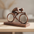 Radfahrer-Statue in Kupfer-Bronze-Optik, Seitenansicht der Rennrad-Pose auf Holzoberfläche, weich unscharfer warmer Hintergrund – Münch3D