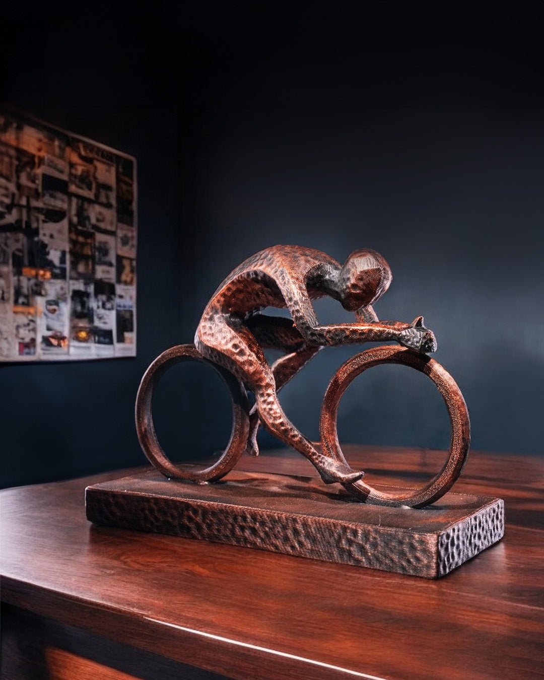 Handbemalte Radfahrer-Statue in Kupfer-Bronze-Optik – Lifestyle-Aufnahme auf Holztisch vor dunkler Wand mit Pinnwand