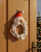 Weihnachtsmann Bart-Kranz mit roter Zipfelmütze und weißem geflochtenem Bart, an heller Holztür mit sichtbarem Aufhänge-Haken, weichem Kontaktschatten auf der Tür, warmem Sonnenlicht von links und Tannengrün mit Lichterkette im Hintergrund