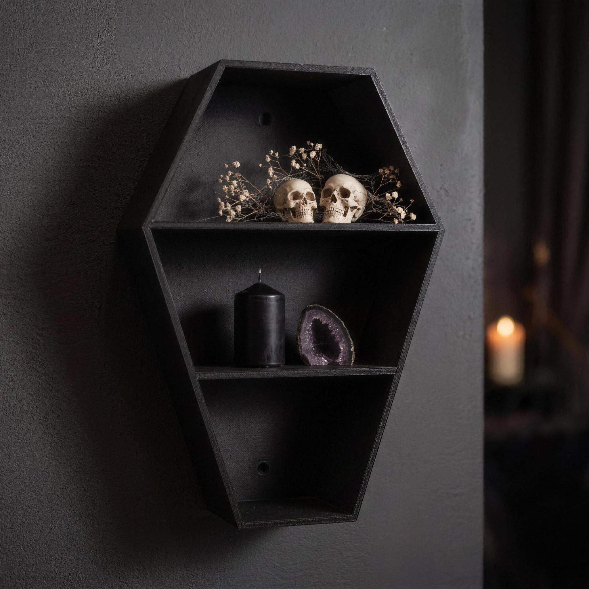 Coffin shelf with two skulls among dried flowers, a black candle and a purple amethyst crystal