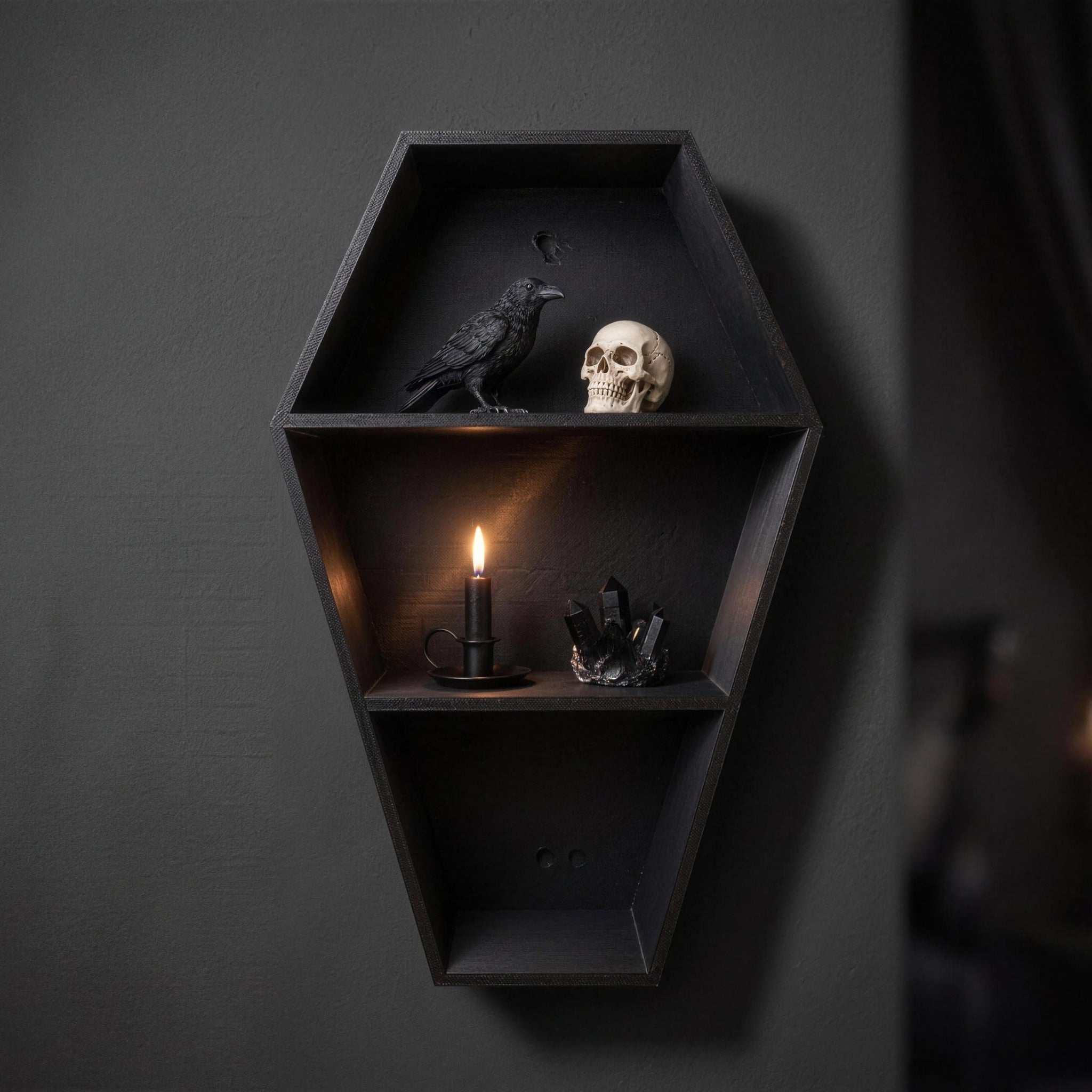 Close-up of coffin shelf with a raven figurine, a skull, a black candle in a candle holder and a black crystal cluster