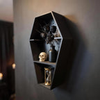 Coffin shelf from a side angle with wilted black roses in a vase, a skull and a gold-framed hourglass