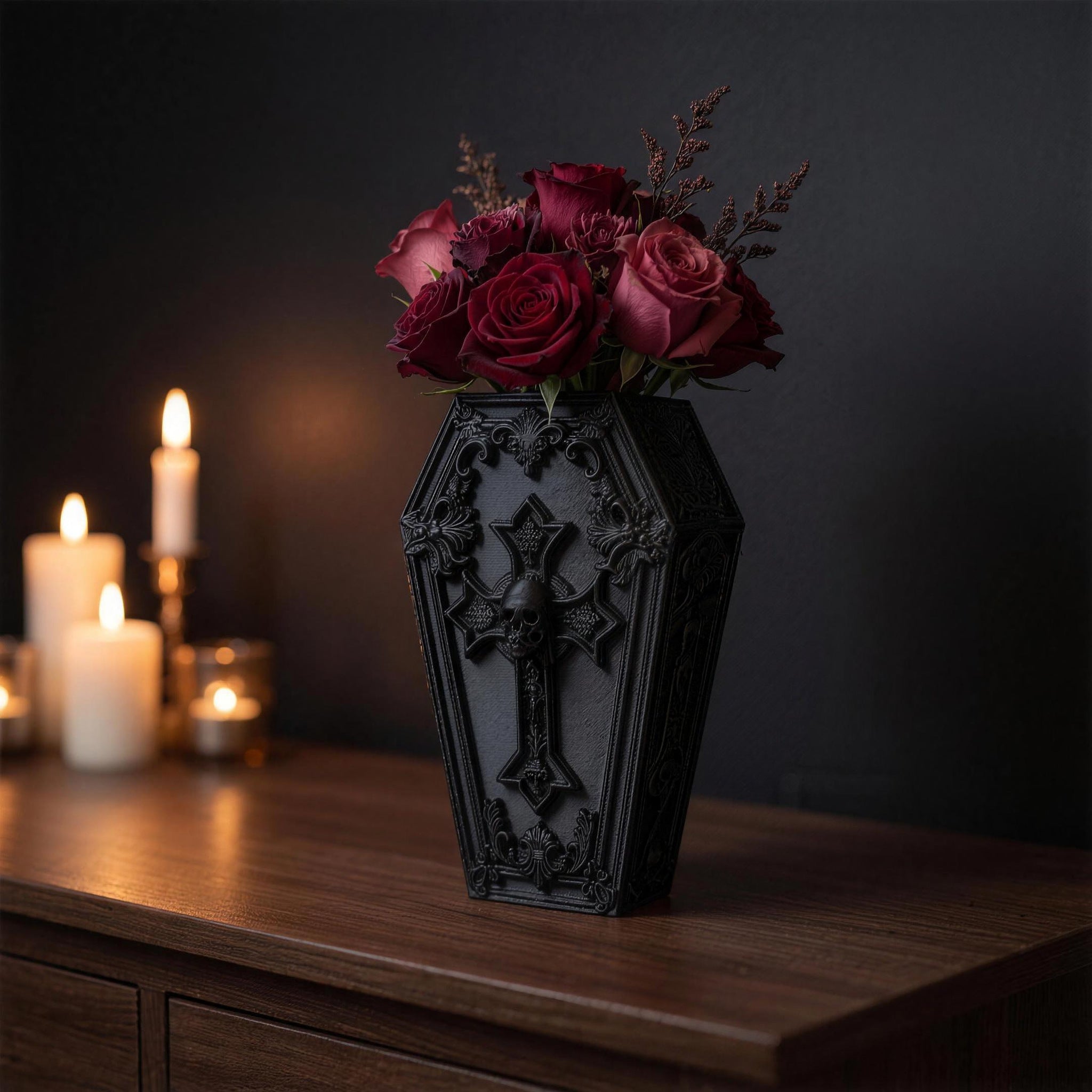 Gothic Sargvase in Schwarz mit Kreuz und Totenkopf-Detail, Frontalansicht mit Rosen und Trockengrün, mehrere Kerzen im Hintergrund