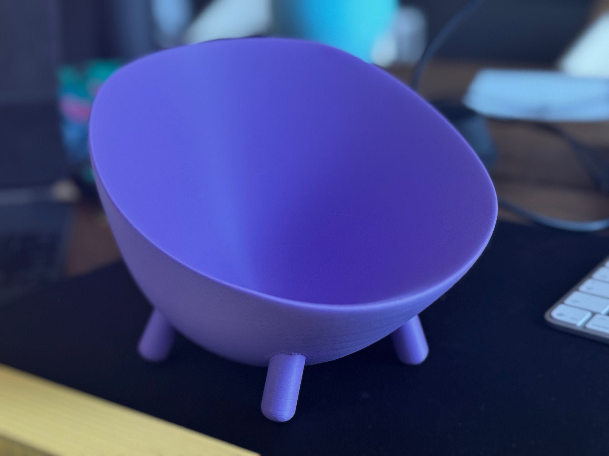Fertig gedruckte lila Schale mit Füßen, unbefüllt, auf dunklem Schreibtisch neben Tastatur, im Hintergrund unscharfes blaues Licht und Monitor.