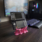 Nahaufnahme des pinken Tropfen-Konsolenhalters aus 3D-Druck mit Steuerkreuz und Actionknöpfen der aufgestellten Handheld-Spielkonsole im Vordergrund, dahinter eine beleuchtete Gaming-Tastatur