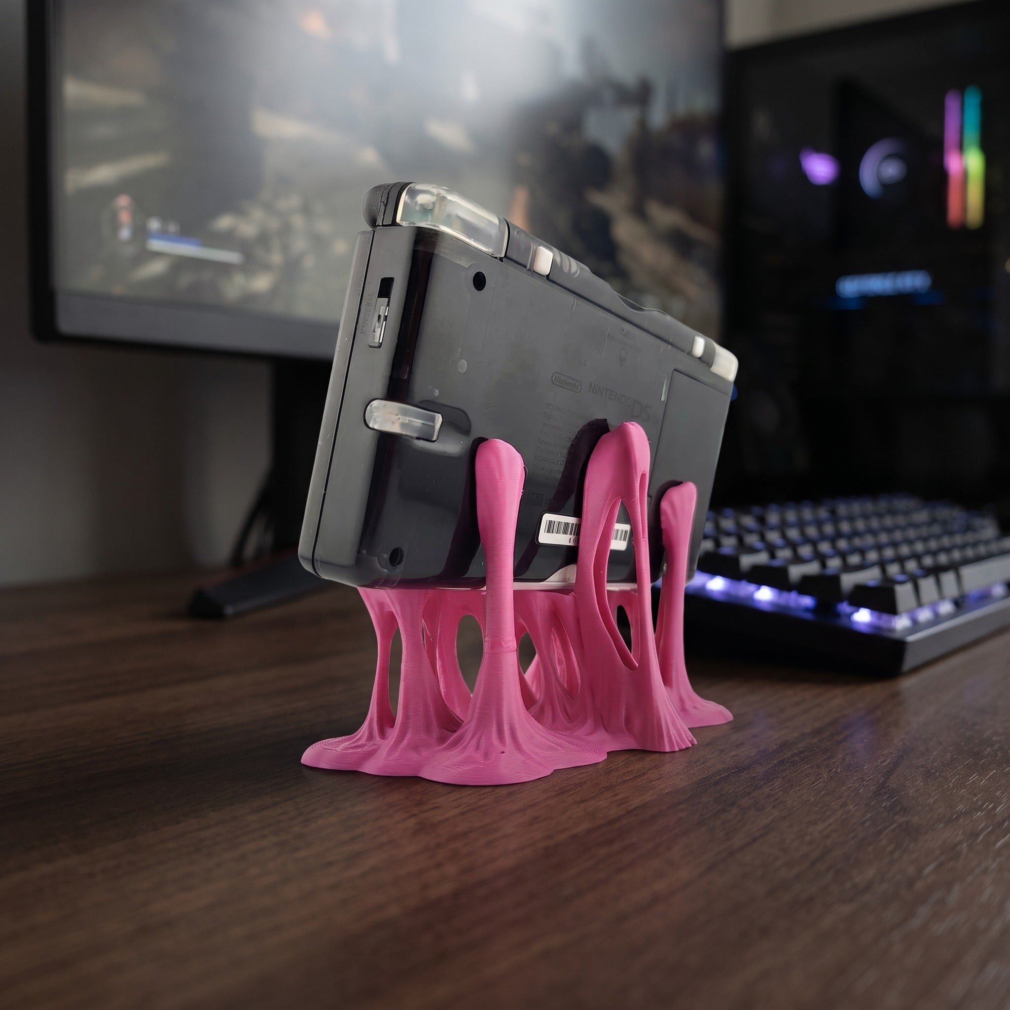 Nahaufnahme der tropfenförmigen, durchbrochenen Standfüße des pinken 3D-Druck-Konsolenhalters von hinten, die die Rückseite einer aufgeklappten Handheld-Spielkonsole stützen