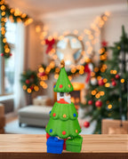 Pop-up-Weihnachtsbaum mit verstecktem Weihnachtsmann, Ansicht mit angedeutetem Motiv, auf Holzregal, weihnachtliche Girlande und Lichterkette im Hintergrund