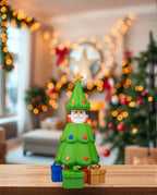 Pop-up-Weihnachtsbaum mit verstecktem Weihnachtsmann, geöffnete Ansicht von vorne, auf Holzregal, weihnachtliche Girlande und Lichterkette im Hintergrund