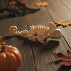 Skelett-Chamäleon-Figur in Detailaufnahme mit Fokus auf dem spiralig eingerollten Schwanz im Vordergrund, Helmkopf im Hintergrund, Halloween-Tischdeko mit Kürbis und Spinnennetz