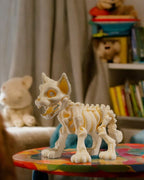Skelett-Katze-Figur in Elfenbein steht auf einem bunten Tisch in einem gemütlichen Wohnzimmer mit Bücherregal im Hintergrund