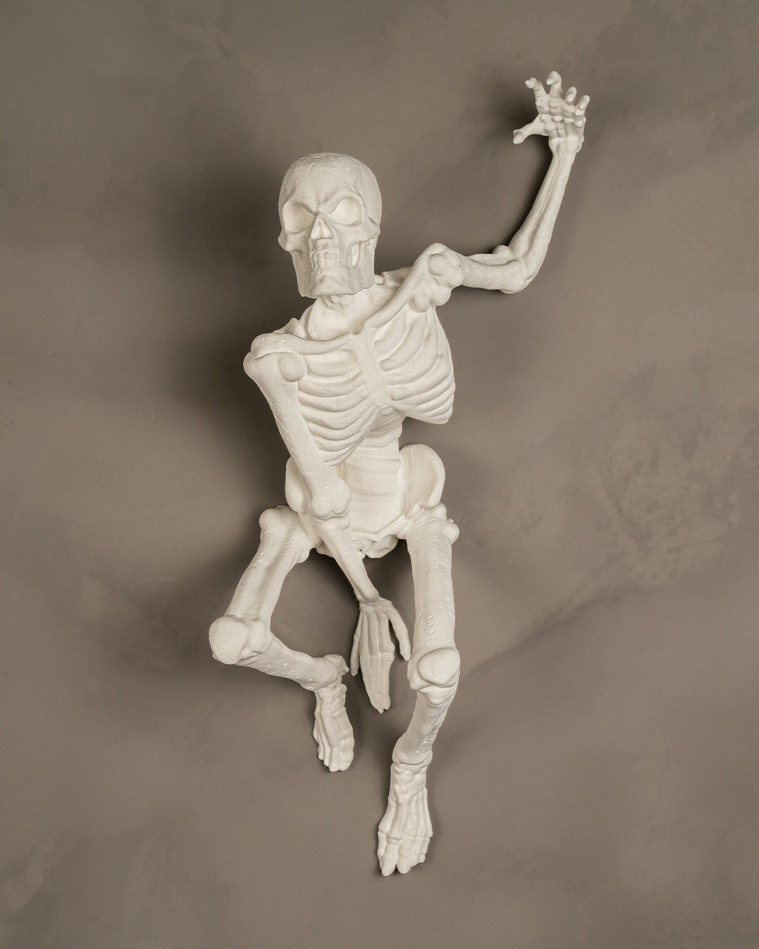 Skelett-Wanddeko 'The Skull' in reinem Weiß, kletternde Pose an grauer Wand montiert