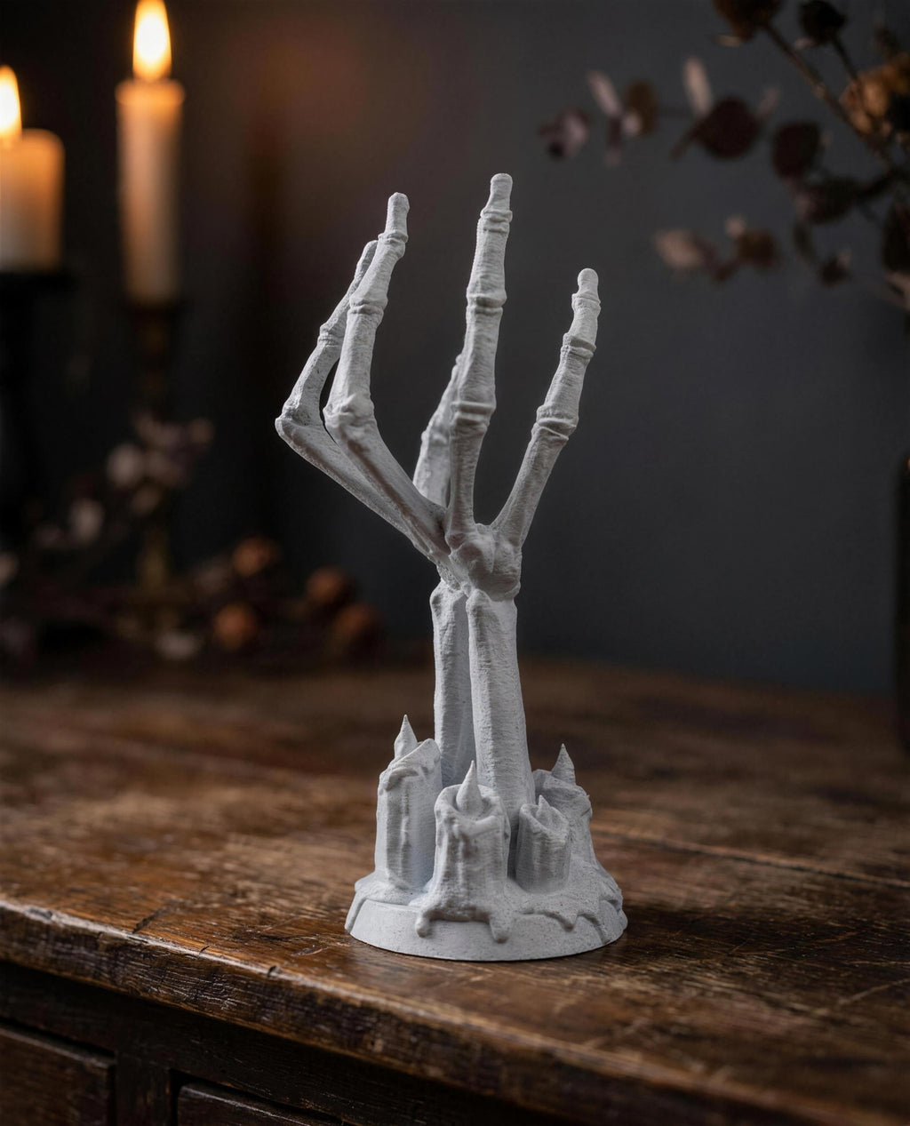 Frontalansicht des Skeletthand-Kerzenhalters ohne Glas auf dunkler Holzkommode mit Kerzen und getrockneten Blumen