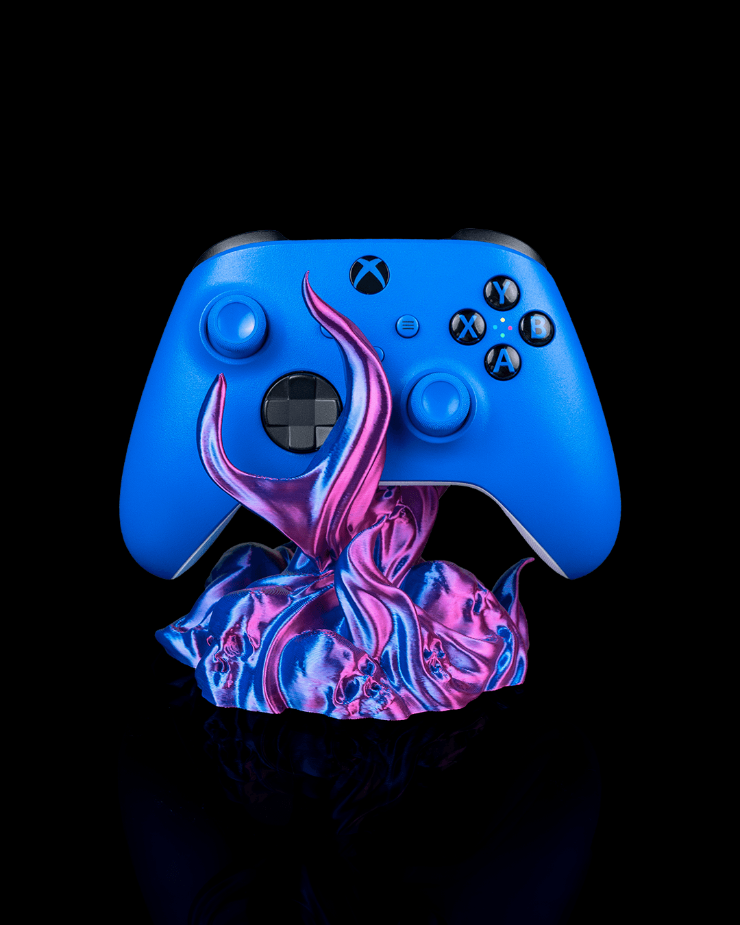 Skullflame Controller-Halter mit blauem Gaming-Controller, Frontalansicht freigestellt vor schwarzem Hintergrund, pink-lila-blauer Flammen-Sockel mit Totenkopf-Reliefs.